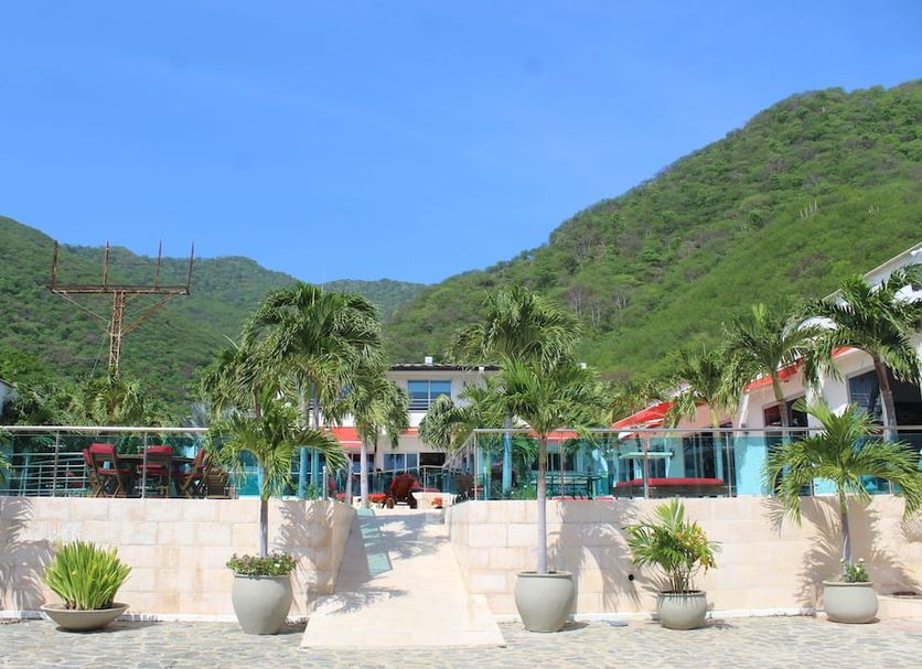 Hotel Kaamú Taganga exterior with palm trees, terrace, and green mountain backdrop