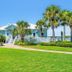 Pinnacle Port A-305 in Panama City Beach with a pastel beach house, palm trees, and lush lawn