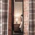 Qudos Salisbury: narrow mirror reflecting bedside lamp, bed and plaid curtains against exposed brick wall