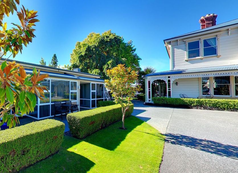 Merivale Manor in Christchurch with manicured gardens, hedge-lined lawn, and a sunny driveway