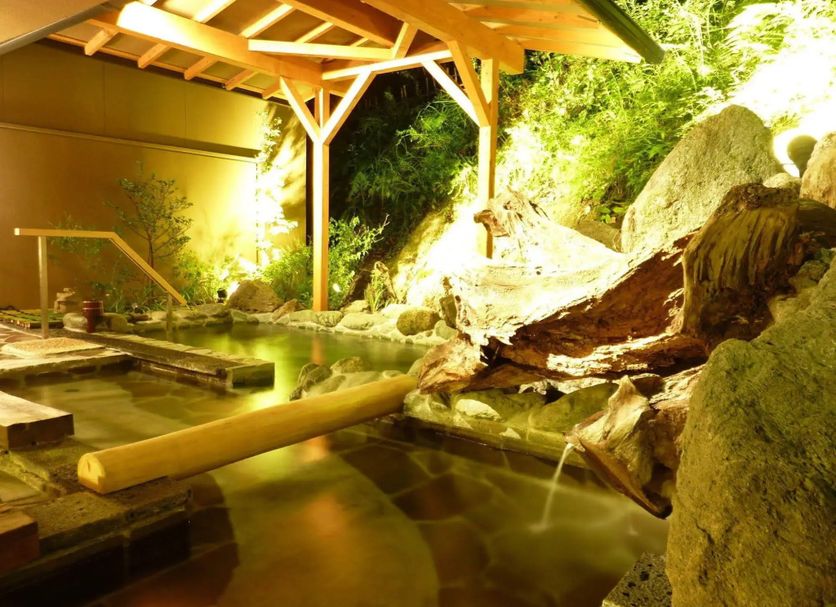 Kameya Ean in Izu features a serene hot spring bath with wooden beams and rock landscaping.