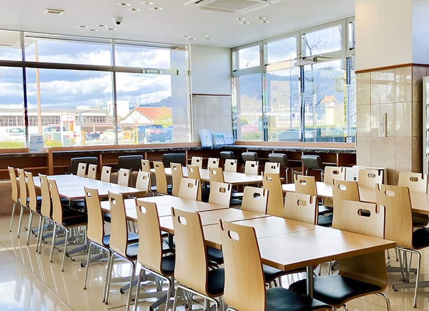 Toyoko Inn Higashi hiroshima Ekimae dining area with long tables, chairs, and large windows in Higashihiroshima