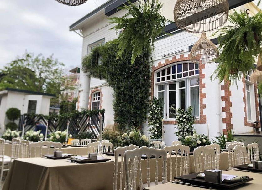 Serguzest Otel in Şekerpinar with an outdoor dining area and hanging plants beside a white building