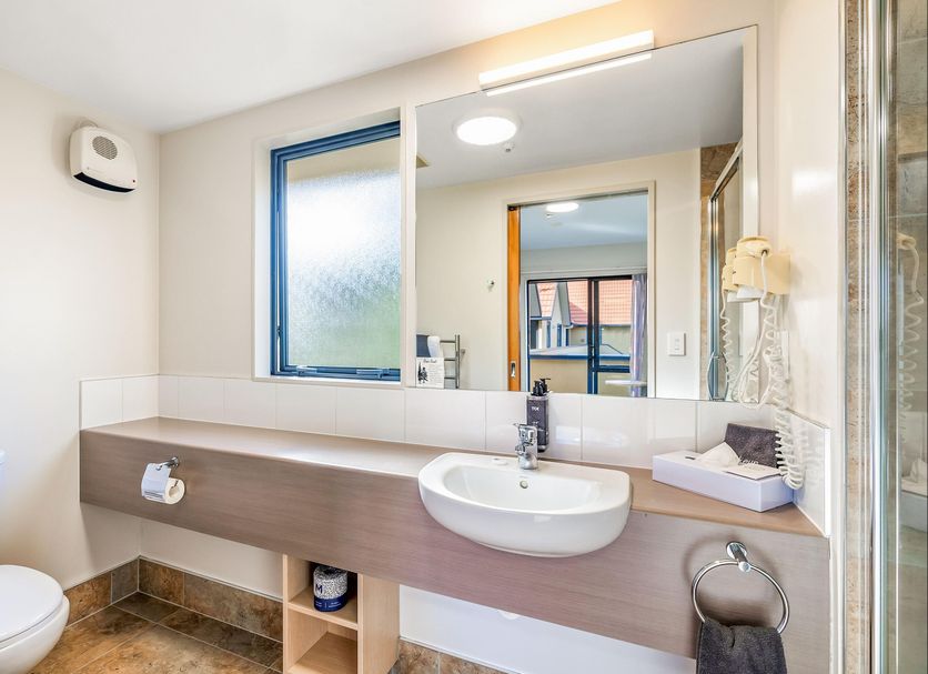 Bathroom at Bella Vista Motel Whangarei with sink vanity, toilet, mirror, and frosted window.