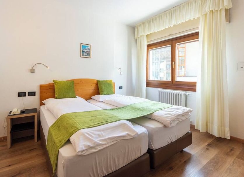 Hotel Oswald in Canazei guest room with twin beds, green accents, and a window with curtains