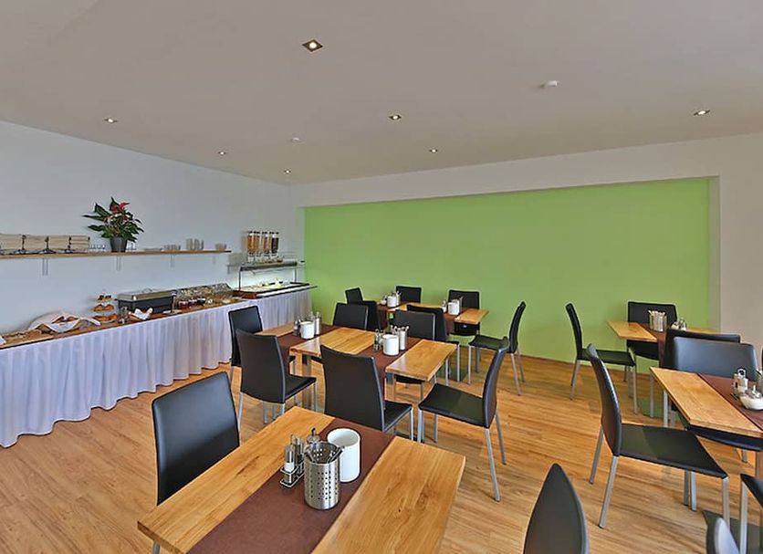 Montagehotel Business & City Linz breakfast room with tables, chairs and buffet against green wall