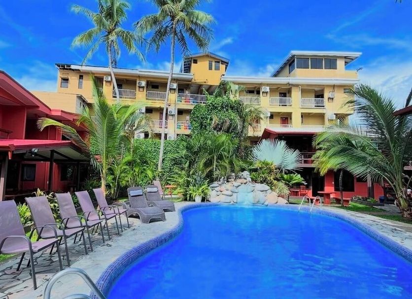 Hotel Los Ranchos in Jacó with tropical pool, lounge chairs, palm trees and colorful buildings