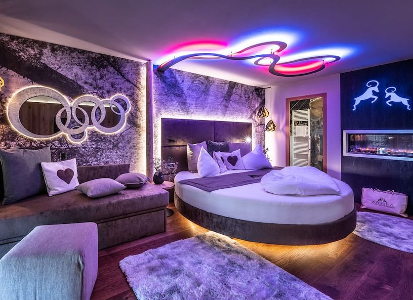 Abinea Dolomiti Romantic Spa in Castelrotto: neon-lit suite with round bed, chaise lounge and wall fireplace