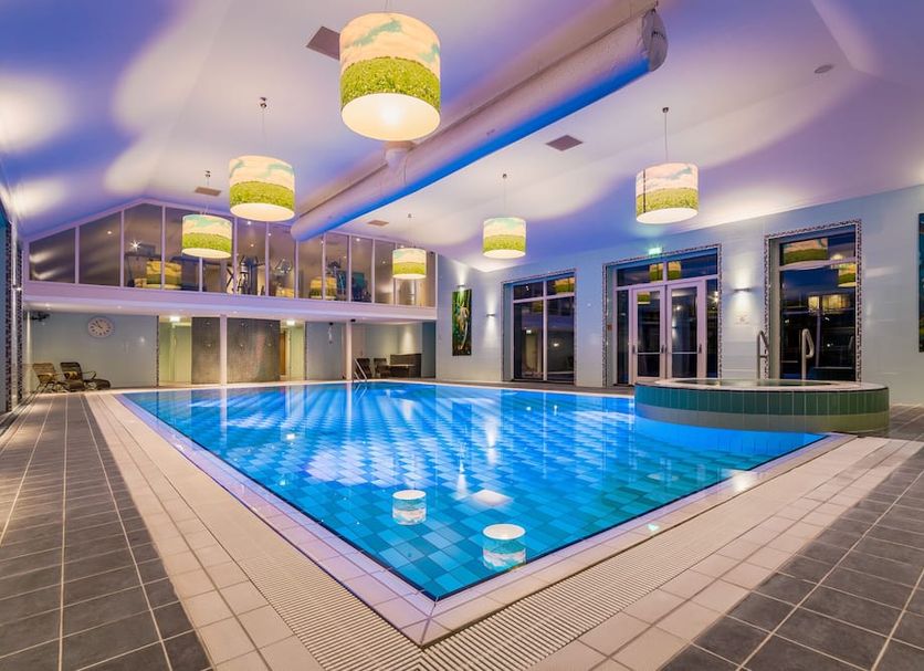 Van der Valk Hotel Emmen indoor pool with blue-lit water, lounge windows, and hanging pendant lights
