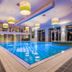 Van der Valk Hotel Emmen indoor pool with blue-lit water, lounge windows, and hanging pendant lights