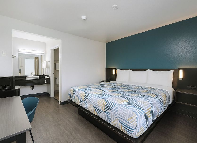 Motel 6 Westminster North guest room with king bed, teal accent wall, desk, and bathroom vanity
