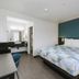 Motel 6 Westminster North guest room with king bed, teal accent wall, desk, and bathroom vanity