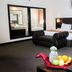 The BCC Hotel & Residence in Batam guest room with king bed, bench, and fruit arrangement