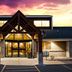 AmericInn by Wyndham Menomonie entrance at sunset with lit lobby and peaked roof