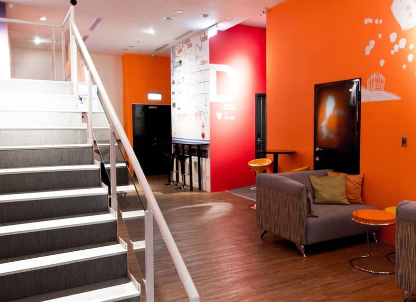 Sleepbox Hostel Taipei City lobby with stairs, orange walls, lounge chairs and a TV