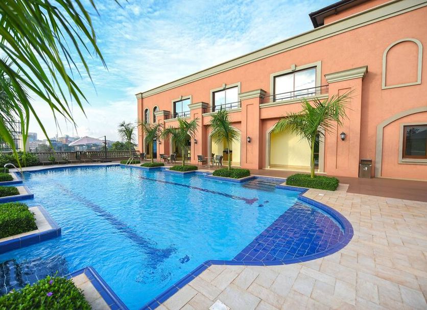 Mestil Hotel & Residences in Kampala with a palm-lined outdoor swimming pool beside a peach-colored building
