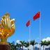 60 West Hotel Hong Kong with golden flower sculpture, palm trees, and Chinese flags against blue sky