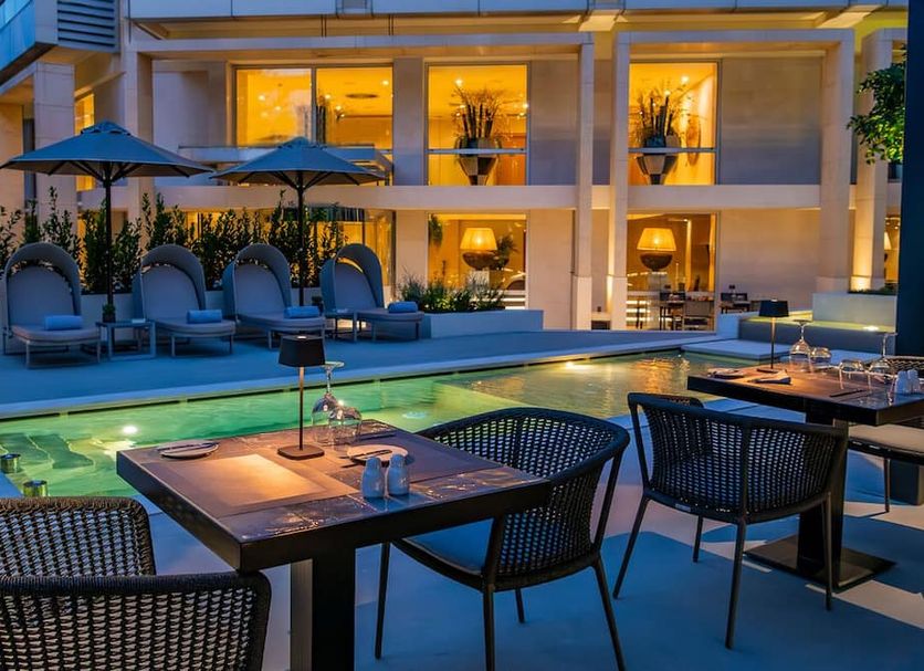 Divani Escape, Vouliagméni: illuminated outdoor pool terrace with dining tables and lounge chairs