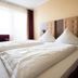 Europa Kehl Hotel guest room with twin beds, tufted headboards, window light and an armchair in Kehl