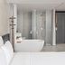 Triple E Hotel Metro Ben Thanh bathroom with freestanding tub, glass shower, and partial bed view in Ho Chi Minh City