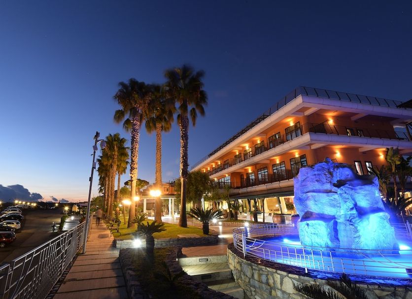 Gli Dei in Pozzuoli at dusk with palm-lined terrace and blue-lit fountain beside the hotel