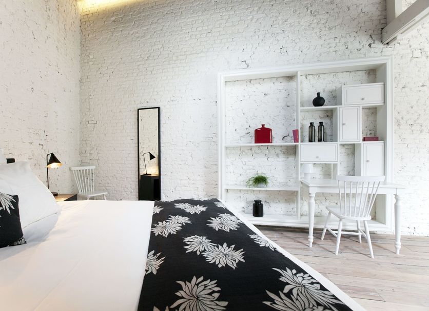 Maison Nationale Antwerp guest room with white brick walls, black-and-white bed, desk and shelving
