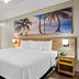 Days Inn by Wyndham Jacksonville NC guest room with king bed, bench, and beach palm wall art