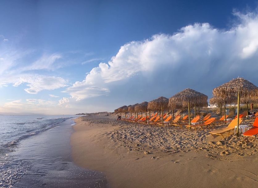 Plaza Beach Hotel in Plaka with beachfront loungers and umbrellas along a sandy shore at sunset
