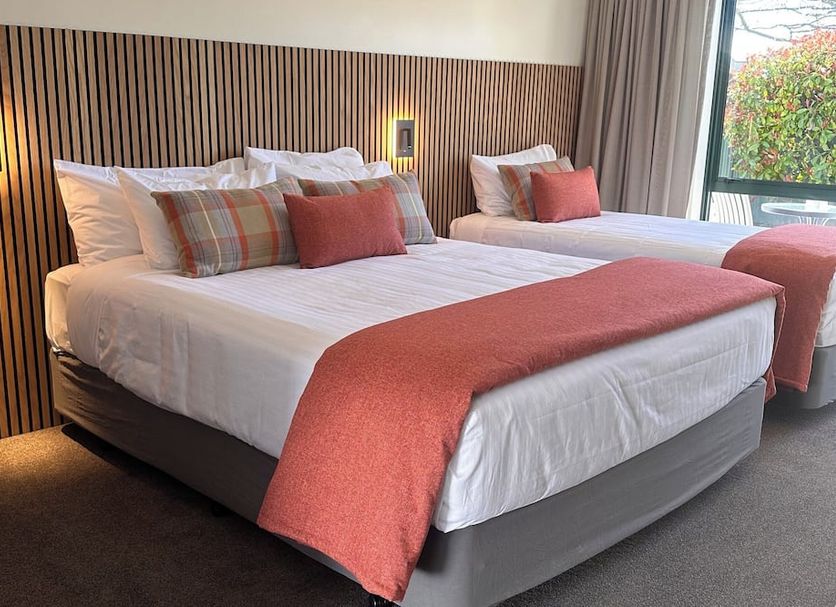 The Lakes Motel Twizel in Twizel room with two neatly made beds beside a window and wood-paneled wall