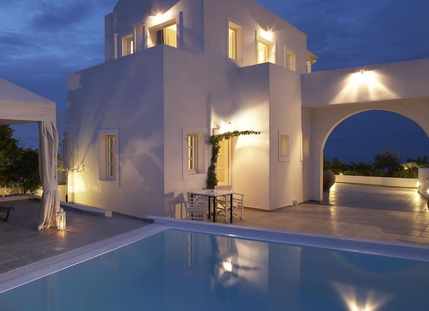 Meli Meli in Thera with a lit white courtyard, pool, and arched terrace at dusk