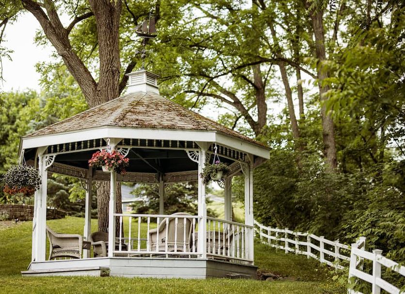 Hudson Manor Bed & Breakfast in Watkins Glen: white gazebo in a garden with hanging flowers and white fence