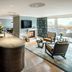 Hotel Bareiss in Baiersbronn: elegant suite with bar, fireplace, seating area and forest-view windows