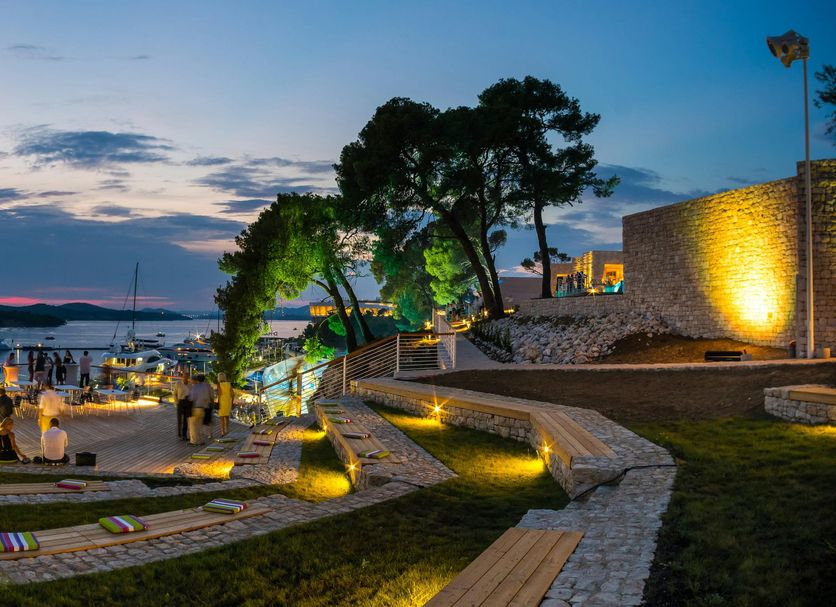 D-Resort Sibenik in Šibenik with a lit waterfront terrace, sea view, and sunset sky