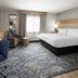 Candlewood Suites Williamsport guest room with king bed, desk, armchair, window, and patterned carpet