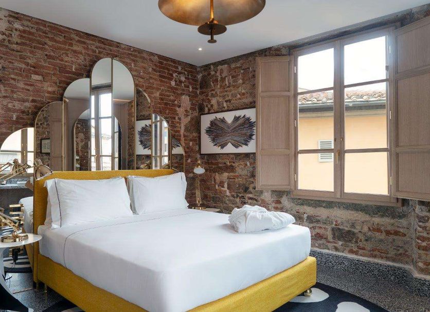 Hotel Calimala Florence room with exposed brick walls, yellow bed, arched mirrors and open window in Florence