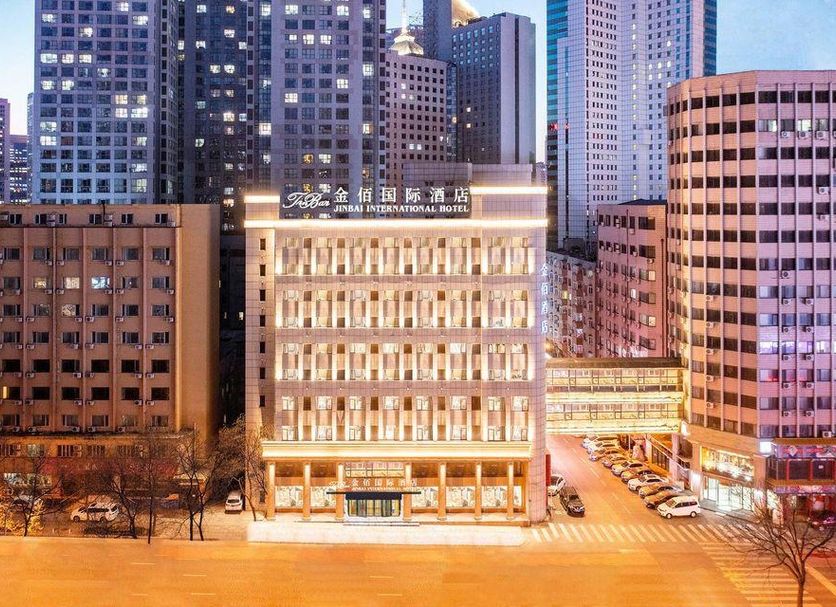 Dalian Jinbai International Hotel in Dalian, city-center façade lit at dusk amid high-rises