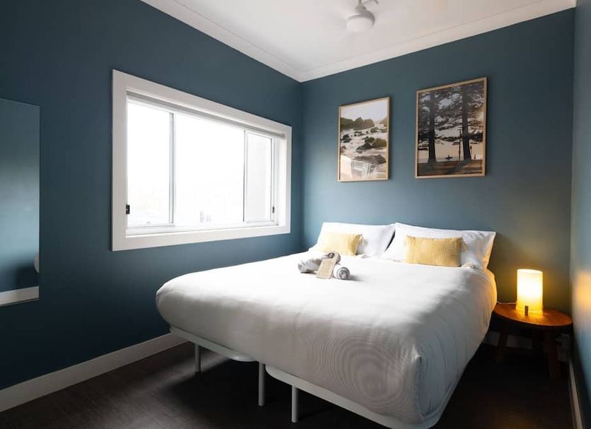 Stoke Beach House Sydney guest room with queen bed, teal walls, window and bedside lamp