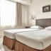 Grand Cikarang Hotel in Bekasi: twin beds in a simple guest room with wall lamps and window light