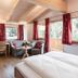 Landhotel Föhrenhof Ellmau guest room with double bed, sofa seating, wood ceiling, and large windows