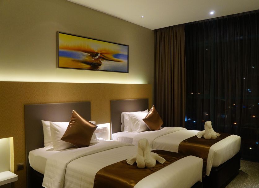 Greens Hotel & Suites Bintulu twin beds with brown accents and city view through large window