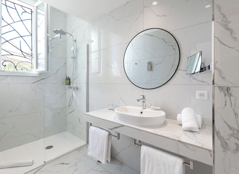 Hotel La Villa Juan Beach bathroom in Antibes with marble tile, round mirror, and walk-in shower