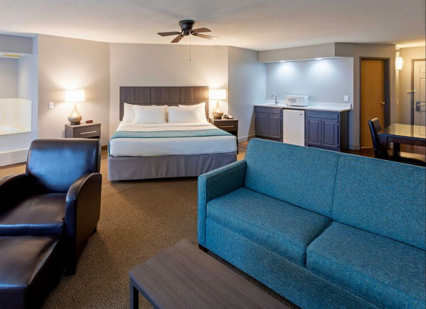Paynesville Inn And Suites guest room with king bed, teal sofa, and black lounge chair in Paynesville