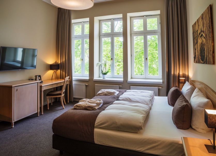 Upstalsboom Heringsdorf room with double bed, desk, TV and large windows overlooking greenery