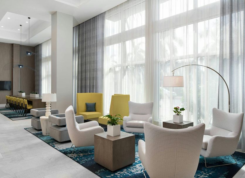 Courtyard by Marriott Delray Beach lobby seating area with white chairs, tables and tall windows in Coral Springs
