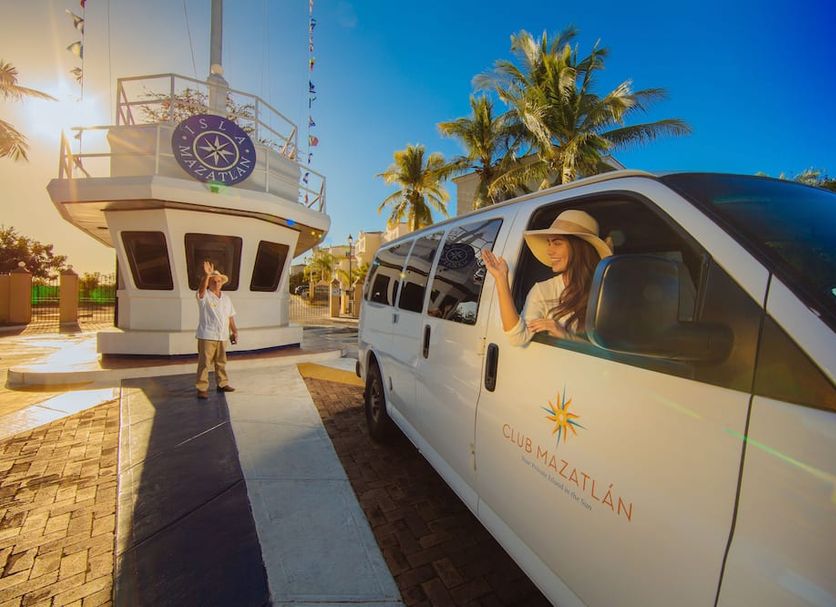 Isla Mazatlan Residence Club in Mazatlán with palm trees and a white shuttle van by a lighthouse-style tower