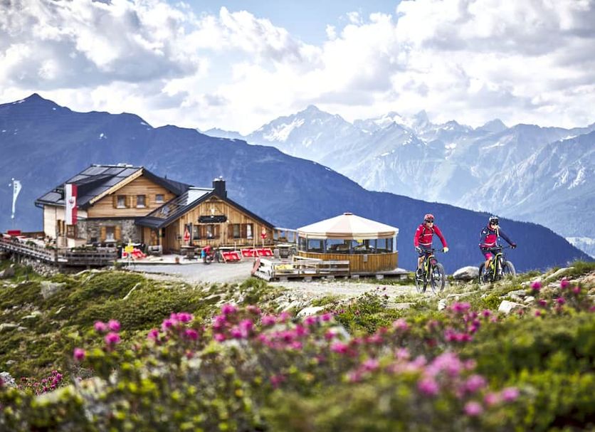 Hotel Alpenkönigin - Alpine Luxury in See with mountain-view terrace and cyclists on a scenic alpine meadow