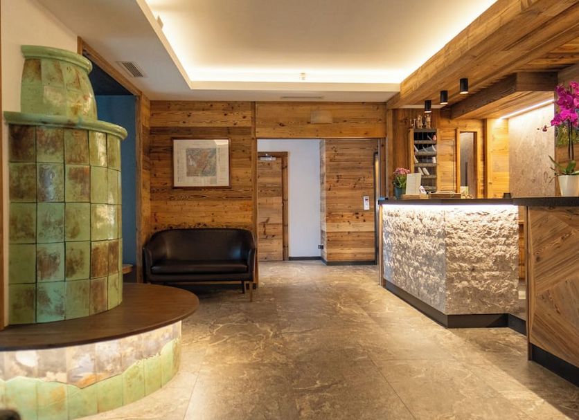 Hotel Ariston S in Madonna di Campiglio: rustic lobby with reception desk and black sofa