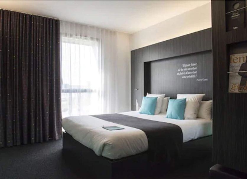 Akena Nantes Atlantis Zénith room in Saint-Herblain with a bed, teal pillows and window curtains
