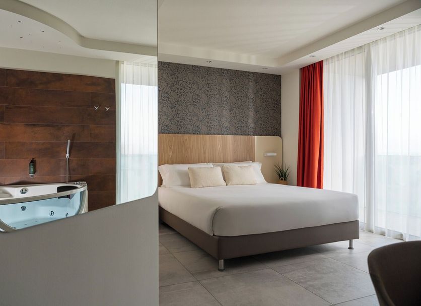 Hotel Aria Rimini guest room with king bed, sliding partition, and bathroom with jetted tub