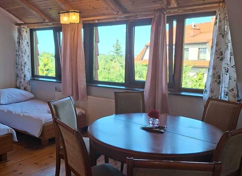 Nowa Villa Zosienka in Gdansk guest room with round table, beds, and large windows overlooking greenery